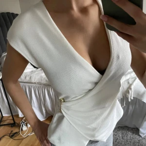 Vit topp Zara  - Jätte snygg omlott topp från Zara med guld spänne. Säljer då den inte kommer till användning. Fint skick då den knappt blivit använd. 
