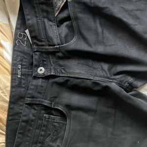 Svarta Replay jeans  - Svarta jeans från Replay i klassisk femficksmodell med snygga detaljer på bakfickorna och Replay-logga på läderpatchen bak. Jeansen har normal passform och är tillverkade i slitstarkt jeanstyg med knapp och dragkedja framtill. Storlek: W 29 men är rätt stor i midjan, L 32 