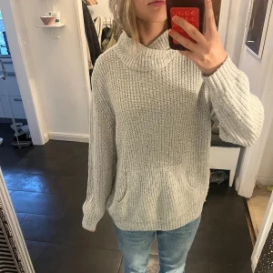 Grå stickad polotröja med fickor - Mysig grå stickad polotröja med bred krage och två praktiska fickor framtill. Tröjan har en loose passform och långa ärmar, perfekt för kyliga dagar. Den ribbade strukturen ger en snygg och avslappnad look.❤️🩶