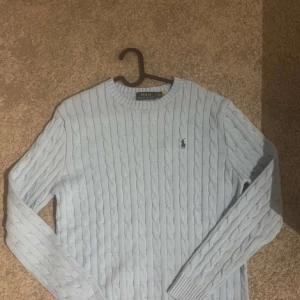 Grå kabelstickad tröja Polo Ralph Lauren - Säljer en ljusblå kabelstickad tröja från Polo Ralph Lauren. Tröjan har rund halsringning, lång ärm och den klassiska broderade loggan på bröstet. Perfekt för dig som gillar stilren och tidlös design.