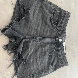 Svarta jeansshorts från Noisy May - Riktigt snygga svarta jeansshorts från Noisy May med råa, fransiga kanter och slitna detaljer framtill. Klassisk femficksmodell med hög midja och knappstängning. Perfekta för en edgy och avslappnad look.