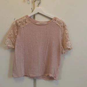 Ljusrosa top med spetsärmar - Säljer en söt ljusrosa top med korta ärmar i blommig spets. Blusen har rund halsringning och är gjord i ett mjukt, tunt material som känns luftigt. Finns ingen storlek men skulle säga att den passar xs/s