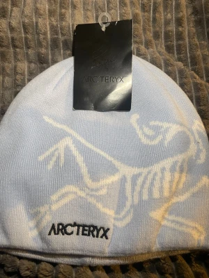 Ljusblå mössa från Arc'teryx - Säljer en ljusblå mössa från Arc'teryx med deras ikoniska fossil-logga i vitt. Mössan är ribbstickad och tillverkad i 100% akryl, vilket gör den mjuk och bekväm. Perfekt för kalla dagar och snygg till streetwear-looken.
