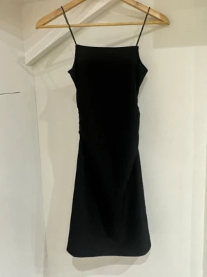 Svart glittrig klänning H&M Divided - Säljer en svart glittrig klänning från H&M Divided i storlek XXS. Klänningen har smala axelband, rak halsringning och är figurnära med lätt rynkade detaljer på sidan. Perfekt för dig som vill ha en enkel men snygg look.