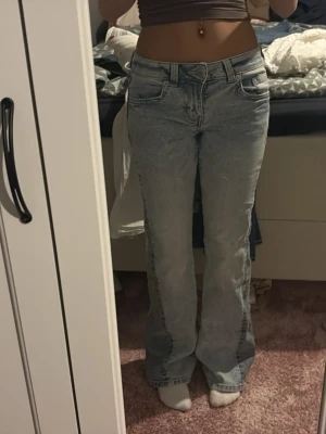 Ljusblå bootcut jeans med fickdetalj - Säljer ett par ljusblå bootcut jeans med snygg tvätt och ficka med knapp bak. Klassisk femficksmodell och normal passform. Jeansen har en lätt utsvängd siluett och är perfekta till sneakers eller boots. Materialet är jeans i bomull.