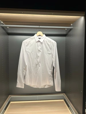 Vit skjorta från Enos Jeans Project - Klassisk vit skjorta från Enos Jeans Project med lång ärm och knappar framtill. Skjortan har en stilren krage och är tillverkad i mjuk bomull som känns skön mot huden. Perfekt för dig som gillar en clean och enkel look.