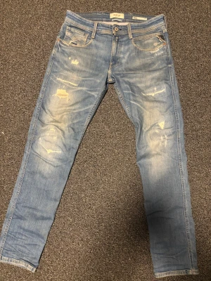 Replay Anbass ljusblå jeans - Säljer ett par Replay Anbass Hyperflex jeans i ljusblå tvätt med slitna detaljer och snyggt distressed look. Klassisk femficksmodell med normal passform och raka ben. Materialet är stretchigt jeans för extra komfort. Perfekta för dig som gillar en avslappnad men trendig stil. Orginal tags och påse följes med! Storlek W31 L32