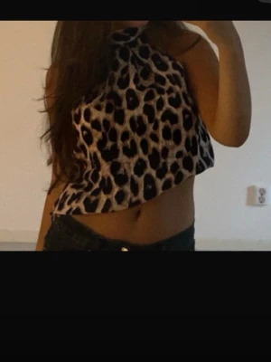 Leopardmönstrad croppad halterneck topp - Säljer en croppad halterneck topp med leopardmönster i beige och svart. Toppen är ärmlös och har hög hals, vilket ger en trendig och edgy look. Perfekt för dig som vill sticka ut och älskar djurmönster.