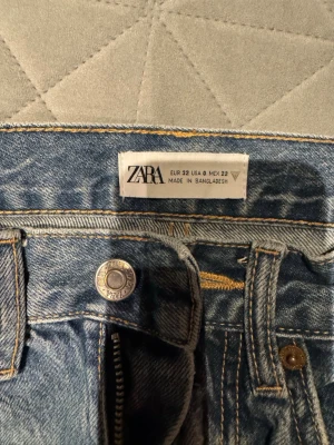 Blå raka jeans från Zara, strl 32 - Säljer ett par klassiska blå jeans från Zara i storlek 32. Jeansen har hög midja, raka ben och femficksmodell med dragkedja och knapp. Materialet är slitstark denim i bomull och färgen är ljusblå med snygg tvätt. Perfekta till sneakers eller boots.
