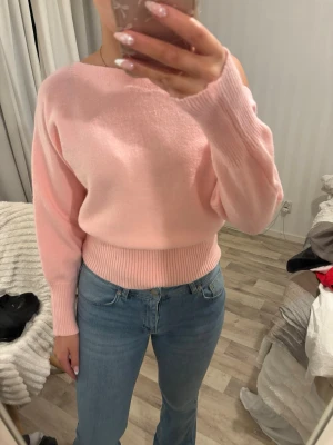 Ljusrosa offshoulder stickad tröja - Supersöt ljusrosa stickad tröja med offshoulder-design och bred ribbad mudd i midjan och vid ärmsluten. Tröjan har en loose passform och är perfekt för dig som gillar en avslappnad men ändå stylish look.