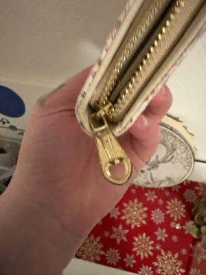 Paris-inspirerad plånbok med blommor - Säljer en ljus plånbok med Paris-motiv, Eiffeltornet, rosa rosor och små guldstjärnor. Plånboken har dragkedja i guld, flera fack för kort och myntfack med dragkedja. Utsidan är dekorerad med ett snyggt spänne och blommigt mönster.