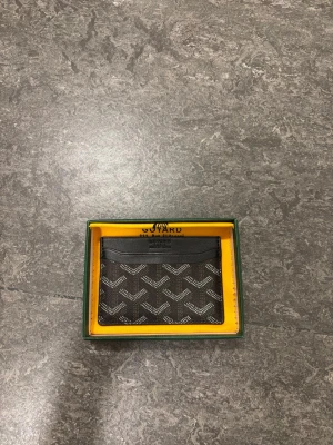 Svart kortfodral  - Säljer ett stilrent svart kortfodral  med en ikoniskt mönster i vitt och grått. Fodralet har flera fack för kort och är tillverkat i skinn.Perfekt för dig som vill ha något både snyggt och praktiskt i fickan.