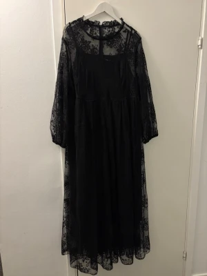 Svart långklänning i spets - Säljer en svart långklänning med transparent spets och blommigt mönster. Klänningen har långärmade ärmar i mesh, rund halsringning och ett tunt innerfoder. Perfekt för dig som vill ha en elegant och unik look.