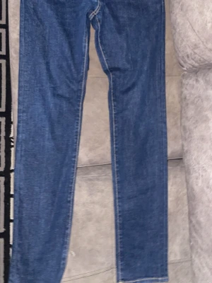 Blå Dsquared2 ICON jeans - Säljer ett par blå jeans från Dsquared2 med klassisk passform och raka ben. Jeansen har tydliga kontrastsömmar, knappgylf och en stor vit 'ICON'-text på bakfickan. Materialet är slitstarkt jeans och märkespatchen sitter bak i midjan.