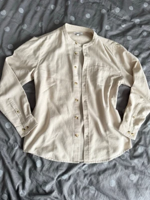 Beige henley-skjorta från Kappahl - Säljer en beige henley-skjorta från Kappahl i mjuk bomull. Skjortan har rundad krage, knappar framtill och en bröstficka. Perfekt för dig som gillar enkel och clean stil.