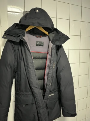 Svart vinterjacka Peak Performance M - Säljer en svart vinterjacka från Peak Performance i storlek M. Jackan har huva, dragkedja och stora fickor framtill. Insidan är vadderad och har snygga röda detaljer. Perfekt för kalla dagar och riktigt skön passform.
