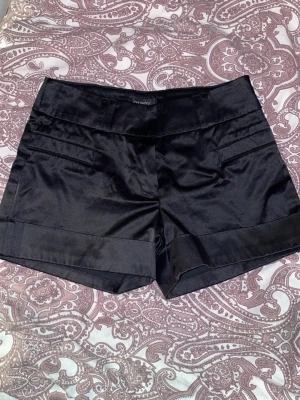 Svarta lågmidjade satinshorts från Orsay  - Säljer snygga svarta shorts från Orsay med bred linning och uppvikta benslut. Säljer pga för små, storlek 36 men passar ej mig som är en 36, midjemåttet är 34 cm rakt över