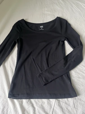 Svart långärmad topp från 157 - En enkel och stilren svart långärmad topp från 157 i storlek XS. Tillverkad i mjuk bomull med lite stretch för skön passform. Perfekt basplagg med rundad halsringning och smal siluett.