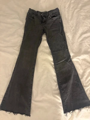 Svarta bootcut jeans från Perfect Jeans - Säljer ett par svarta bootcut jeans från Perfect Jeans i storlek 34. Jeansen har låg midja, klassisk femficksdesign och råa, fransiga benslut för en edgy vibe. Materialet är mjukt jeans med lite stretch för extra komfort.
