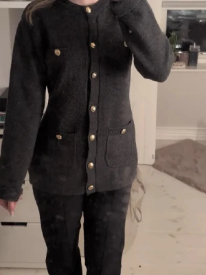 Mörkgrå kofta med guldknappar - Säljer en mörkgrå kofta med snygga guldknappar framtill och på fickorna. Ko crtan har lång ärm, rund halsringning och två fickor fram. Perfekt för dig som gillar klassisk men ändå trendig stil.