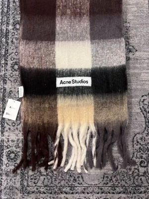 Rutig ullväst Acne Studios - Säljer en rutig väst från Acne Studios i mjuk ullmix. Västen har breda blockrutor i brunt, beige, grått och vitt samt långa fransar nedtill. Perfekt för dig som vill ha en statement piece med klassisk Acne-vibe. Den det går att diskutera pris hör av er