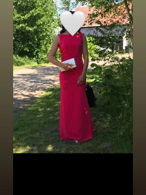 Lång röd klänning med ärmlös design - Säljer en elegant lång röd klänning med figurnära passform och ärmlös design. Klänningen har en enkel, stilren siluett som ger ett sofistikerat intryck. Perfekt för studentbal eller festliga tillfällen.