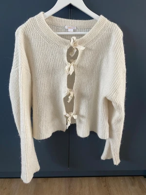 Vit stickad tröja från Gina Tricot - Mysig vit stickad kofta från Gina Tricot med fyra dekorativa knytband framtill. Koftan har lång ärm. Perfekt för lager på lager under kyliga dagar. Sparsamt använd-mycket bra skick. Storlek 170 men motsvarar en S.