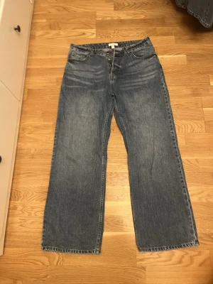 Blå wide jeans från H&M, strl 44 - Säljer ett par blå jeans från H&M i storlek 44. De har en klassisk femficksmodell, raka och vida ben samt normal midja. Jeansen är tillverkade i bomull och har en snygg tvättad look med ljusare partier framtill.