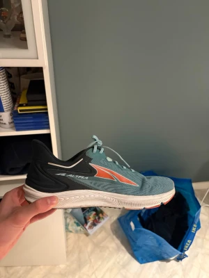 löparskor från Altra modell Torin 6 - Säljer ett par snygga blåa Altra löparskor med vit sula och svarta samt orange detaljer. Skorna har snörning och är tillverkade i ett ventilerande syntetmaterial. Perfekta för dig som gillar att springa eller träna. Skön passform och riktigt sportig!