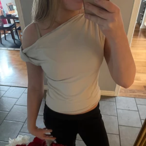 Beige oneshoulder topp från H&M Divided - Säljer en beige oneshoulder topp från H&M Divided i storlek S. Toppen har en tight passform och är tillverkad i mjuk bomullsmix. Toppen kommer tyvärr inte till användning för mig längre💗
