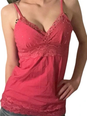 Rosa linnetopp med spets och paljetter - Söt rosa linnetopp med smala axelband, spetsdetaljer vid byst och nederkant samt paljetter på bröstet. Toppen har omlott-skärning framtill och är lätt utsvängd nertill. Perfekt för sommarens alla tillfällen.