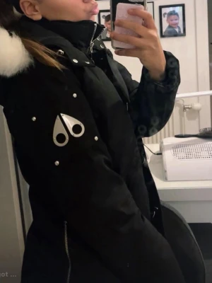 Svart dunjacka med vit pälshuva från Moose Knuckles - Säljer en svart dunjacka från Moose Knuckles med vit pälskant på huvan och ikoniska loggan på ärmen. Jackan har dragkedja, stora knappar och flera fickor. Perfekt för kalla dagar och riktigt snygg streetstil. Priset kan diskuteras 