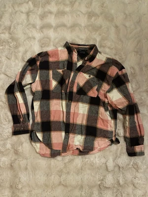 Rutig skjorta från Bluewear, S - Säljer en rutig skjorta från Bluewear i storlek S. Skjortan har stora rutor i rosa, svart, grått och vitt, två bröstfickor med knappar och klassisk krage. Tillverkad i mjuk bomull, perfekt för en avslappnad look.