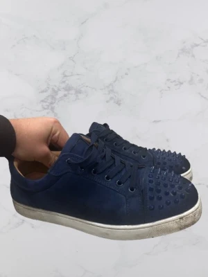 Mörkblå sneakers med nitar från Louboutin - Hej! Jag säljer dessa blåa loubitins, de saknar nitar som man ser i bilderna men det följer med extra nitar på köpte inklusive dustbag, efter en bra tvätt ser dessa extremt rena ut.