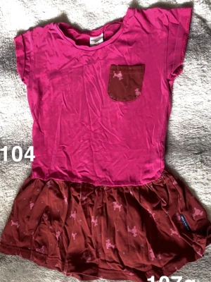 Rosa tunika med ficka och kjoldetalj - Söt rosa topp med korta ärmar. Nederdelen har en kjoldetalj med små rosa hundmönster. Perfekt för dig som gillar färg och lekfulla detaljer.🌸 Fint använt skick. Storlek 104