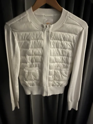 Vit quiltad pufferjacka med dragkedja - Snygg vit pufferjacka med quiltad framsida och två fickor. Jackan har ribbade muddar, lång ärm och hel dragkedja framtill. Använd fåtal gånger. Inga defekter heller💕