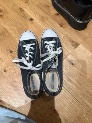 Svarta Converse låga sneakers - Klassiska svarta Converse sneakers med vit tå och vita snören. Skorna har kontrastsömmar och platt sula. Tillverkade i canvas med gummidetaljer. Perfekta för en avslappnad och cool stil.