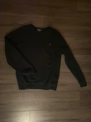 Svart sweatshirt från Polo Ralph Lauren - Klassisk svart tröja från Polo Ralph Lauren med rund halsringning och diskret röd logga broderad på bröstet. Storleken är barn XL så motsvarar ungefär en S. Jättebra skick då den knappt är använd, skriv vid frågor!