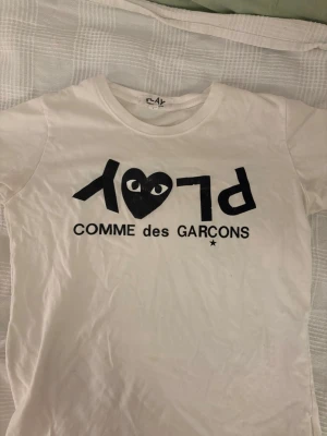 CDG Play t shirt  - Säljer denna T-shirt ifrån Comme Des Garçon då den inte passar mig, med det billiga priset då trycket har slitits efter att ha råkat tvättats i för hög värme. Fortvarande ett värt köp med tanke på det låga priset! Vill bara bli av med tröjan. Storlek S, skriv för frågor!