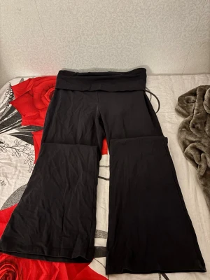 Svarta bootcut mjukisbyxor - Säljer ett par svarta mjukisbyxor med bootcut-modell och bred linning. Byxorna har en skön och stretchig passform, perfekta för chill dagar eller när du vill ha något bekvämt. Materialet känns mjukt och följsamt.