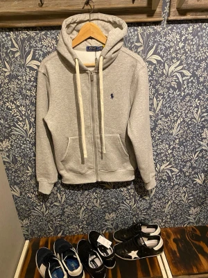 Ralph lauren zip - Grå zip-hoodie från Polo Ralph Lauren med broderad logga på bröstet. Klassisk och bekväm modell.  🧵Helt ny skick  📏 Storlek: M 🎨 Grå 🏷️ Original  Hör av dig vid frågor. Frakt inom 24h🚚🚚