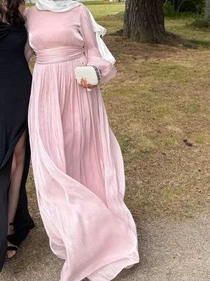 Ljusrosa långklänning med volangärm - Säljer en fin rosa modest klänning som passar perfekt till bal eller bröllop. Klänningen har en osynlig dragkedja baktill och kommer med ett matchande bälte som kan knytas till en rosett, vilket syns på bilden. Klänningen är använd en gång på balen och är i mycket fint skick. Pris: 800 kr + frakt.