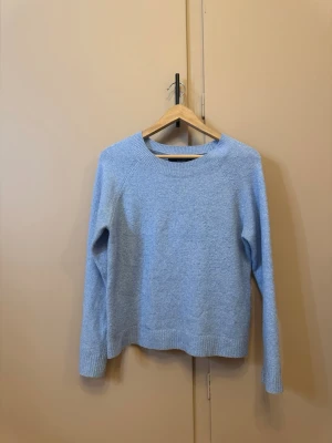 Ljusblå stickad tröja Vero Moda - Mysig ljusblå stickad tröja från Vero Moda i storlek S. Tröjan har rund halsringning, ribbade muddar och är långärmad. Perfekt för kyliga dagar och enkel att matcha med jeans eller kjol.