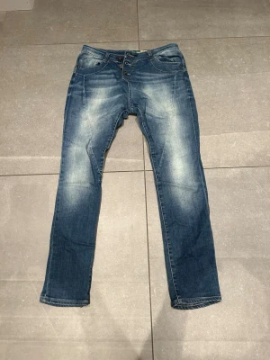 Blå jeans med raka ben och knappar - Säljer ett par klassiska blå jeans med raka ben och snyggt slitna detaljer framtill och baktill. Jeansen har knappgylf och femficksmodell. Materialet är robust denim och passformen är normal. Perfekta till vardagslooken! Hör av vid frågor🤝