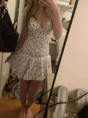 Vit blommig kortklänning med volang - Supersöt vit kortklänning med blått och lila blommönster. 💕