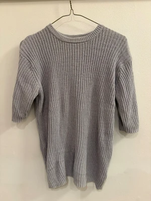 Grå ribbad tröja Carin Wester - Säljer en grå ribbad tröja från Carin Wester med halvkort ärm och rund hals. Tröjan är gjord i mjuk bomullsblandning och har en relaxed fit som passar perfekt till lager på lager. Enkel och stilren design som funkar året runt.