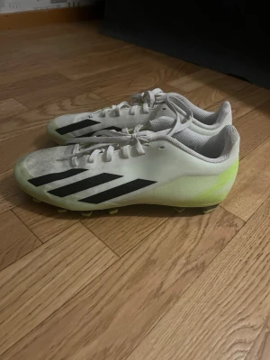 Adidas Crazyfast vita fotbollsskor - Säljer ett par Adidas Crazyfast fotbollsskor i vitt med svarta ränder och limegula detaljer. Skorna har snörning och dobbar för bra grepp på planen. Ovandelen är i syntetmaterial och designen är riktigt sportig och clean.