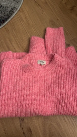 Rosa stickad tröja från ONLY - Supermysig rosa stickad tröja från ONLY med diskret glittrig effekt. Tröjan har rund halsringning och långa ärmar, perfekt för att hålla sig varm under kyliga dagar. Den ribbstickade strukturen ger en snygg och trendig look. Säljer för 100 då den aldrig har använts men pris kan sänkas via snabbaffär!!
