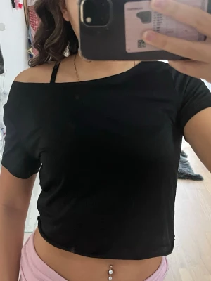 Svart offshoulder croppad topp - Säljer en svart croppad topp med offshoulder-design och korta ärmar. Toppen har en enkel och stilren look. Materialet känns mjukt och stretchigt, troligen bomull eller polyester❤️