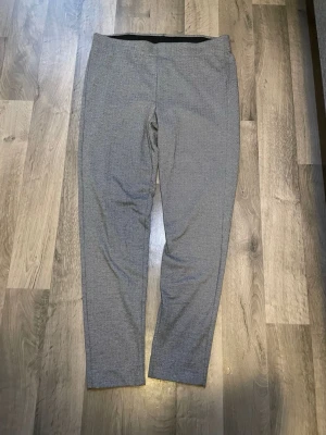 Gråmönstrade kostymbyxor från Yest - Snygga grå kostymbyxor från Yest med diskret fiskbensmönster. Byxorna har rak passform, elastisk midja och är tillverkade i ett mjukt material som ger en bekväm känsla. Perfekta för dig som vill ha en stilren look.